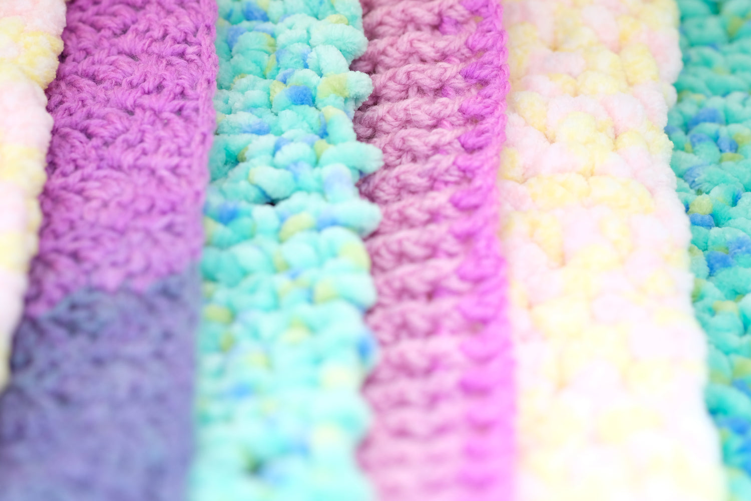 several scarves lined up side by side starting with a yellow and pink dot, purple ribbing, blue-green and purple with blue